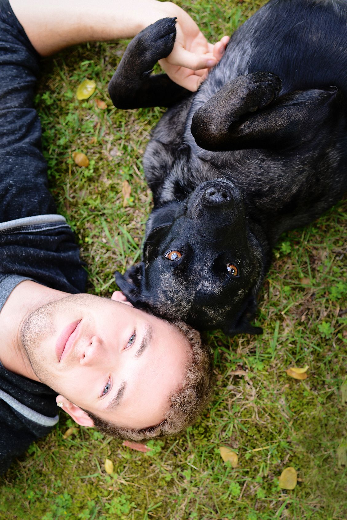 Black dog and companion lying on grass sharing a tender moment outdoors.
