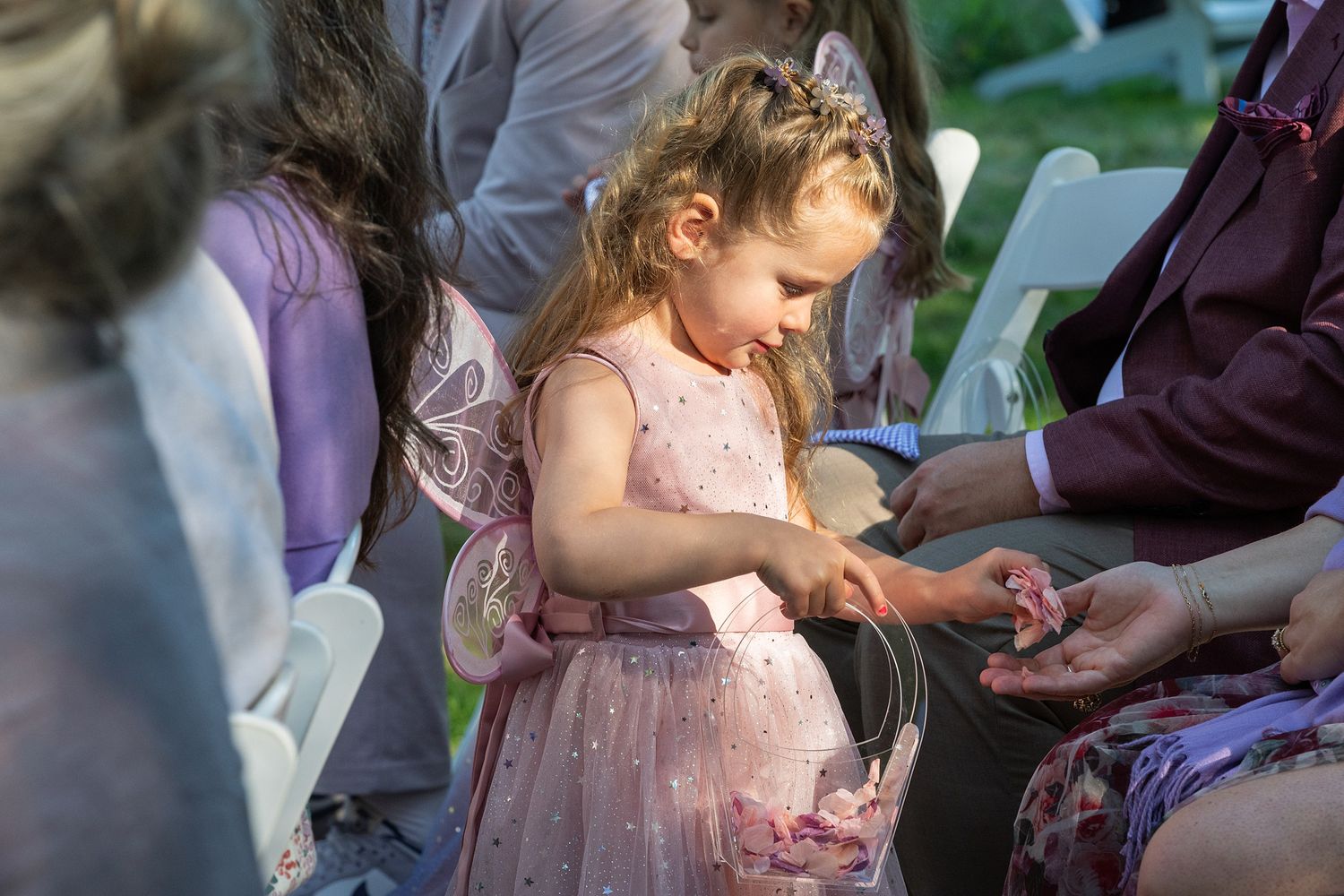 A person in a pink dress at an outdoor wedding reception interacts with guests seated at tables.