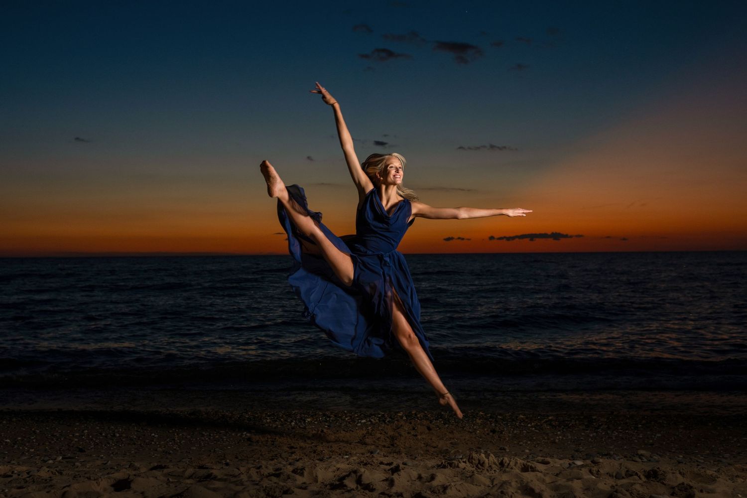 Dancer leaps gracefully on beach during dramatic sunset over ocean.
