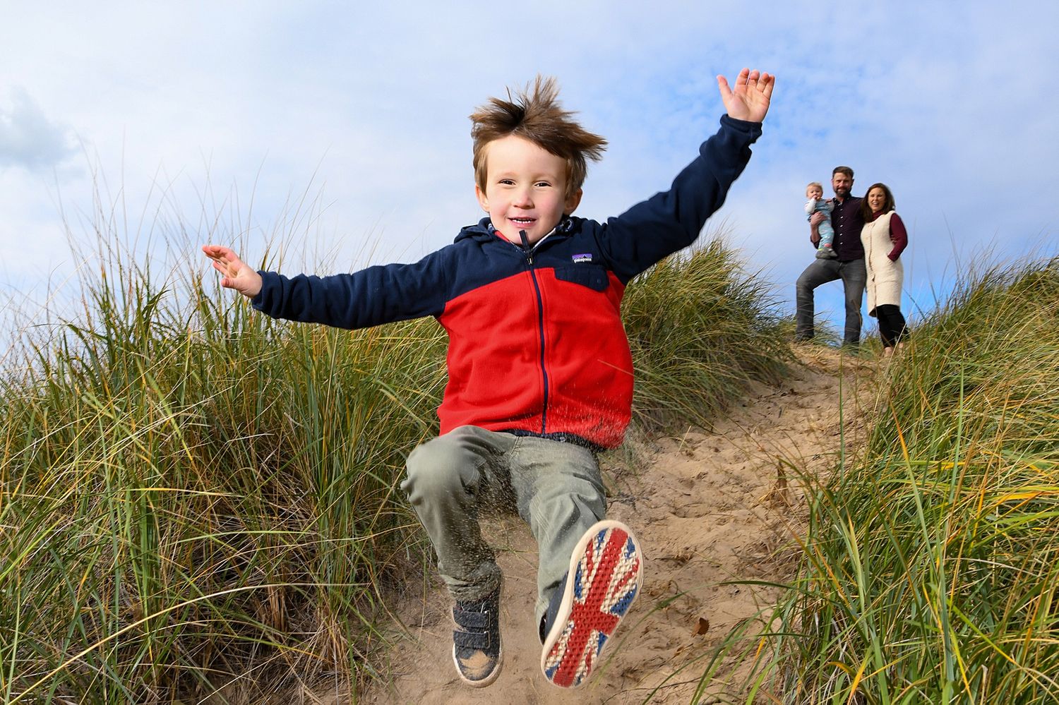 Person jumping joyfully over sand dunes against blue sky background.