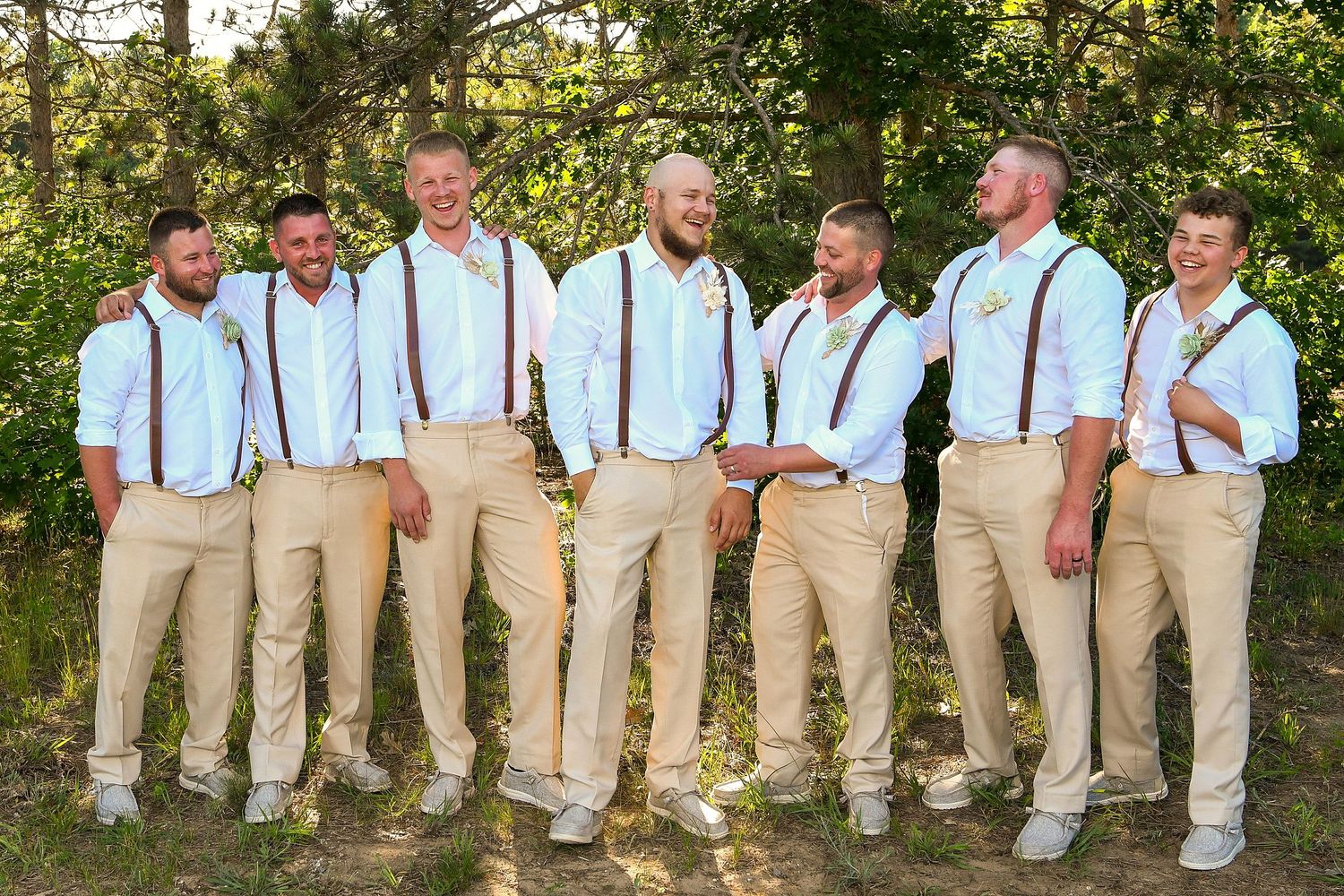 Groomsmen in khaki pants and suspenders pose casually outdoors for wedding party photos.