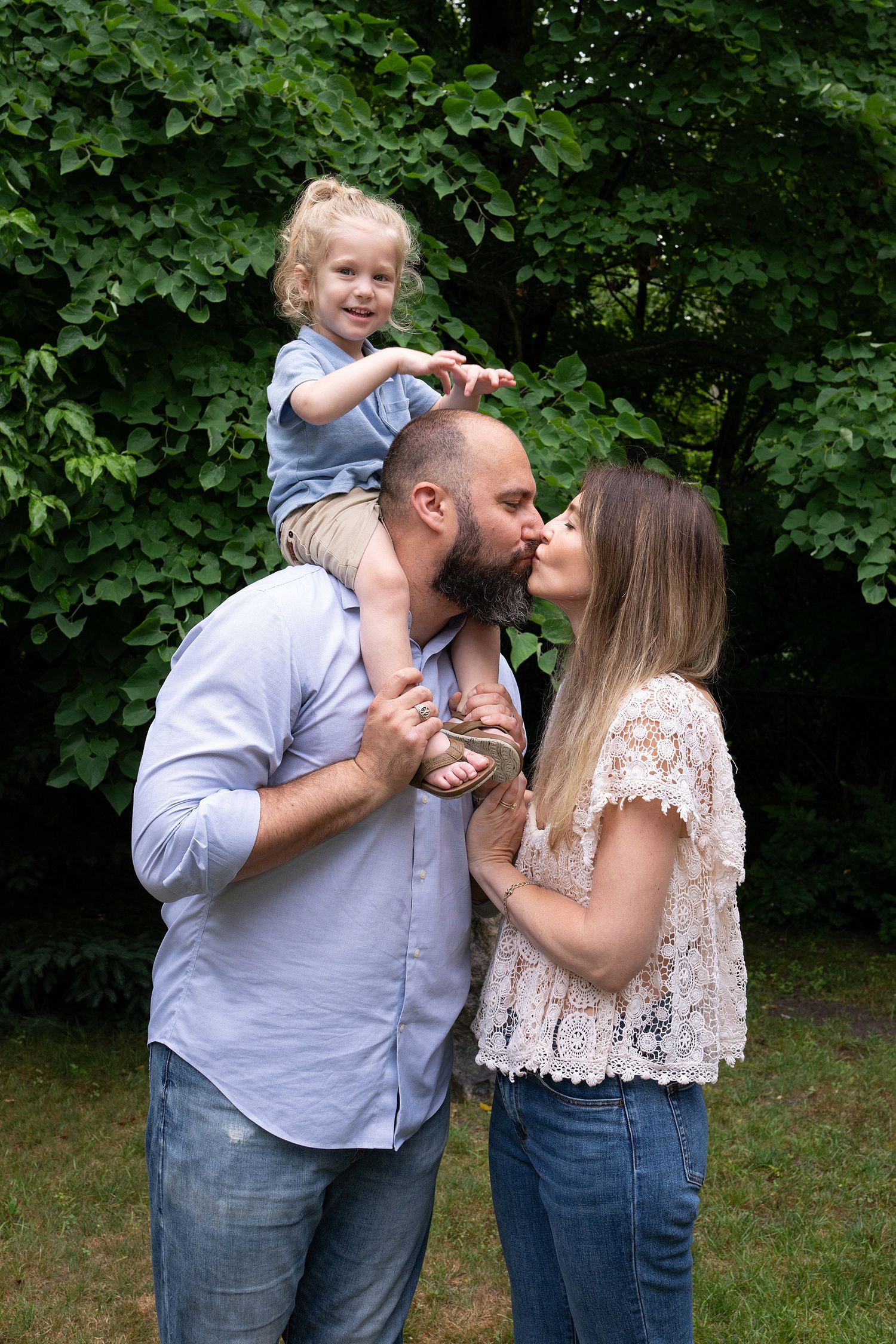 A playful family photo session in a lush green park setting with casual summer outfits.