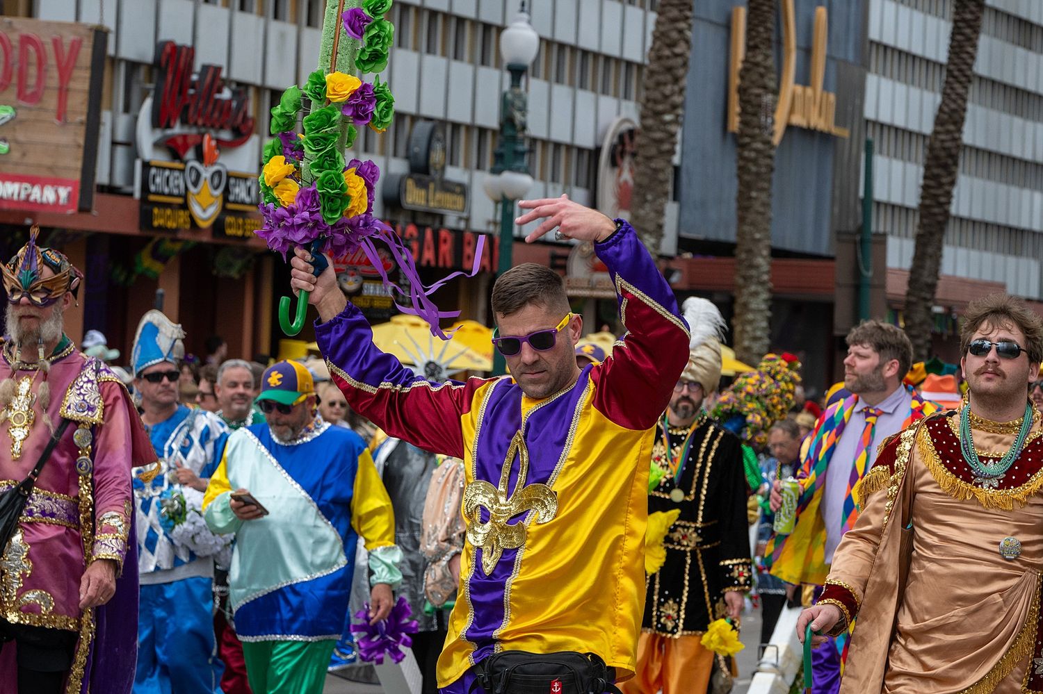 Mardi Gras parade featuring performers in bright yellow and blue costumes walking down the street.