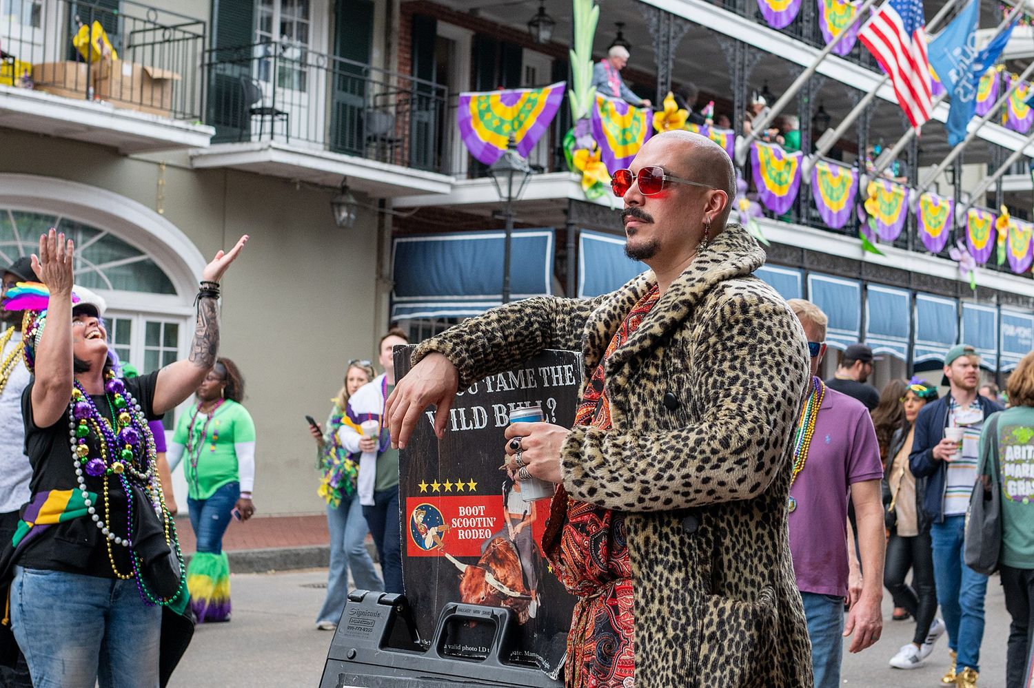 Festive crowd lined up along balconies decorated with flags and Mardi Gras decorations.