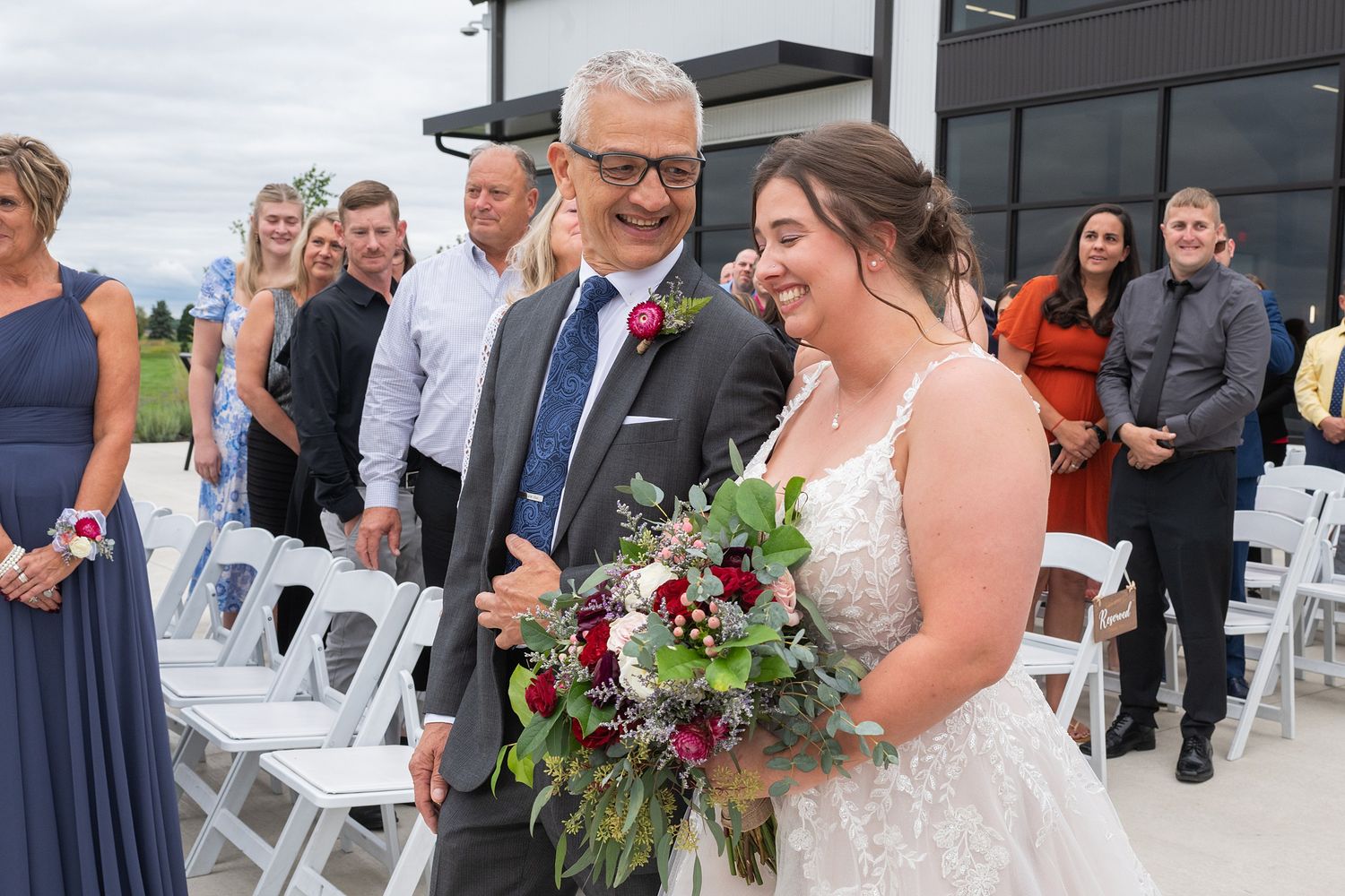 Bride and father share a joyful walk down the aisle surrounded by wedding guests outdoors.