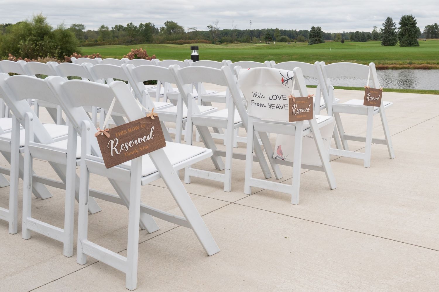 White folding chairs with reserved signs arranged for outdoor wedding ceremony near a pond.