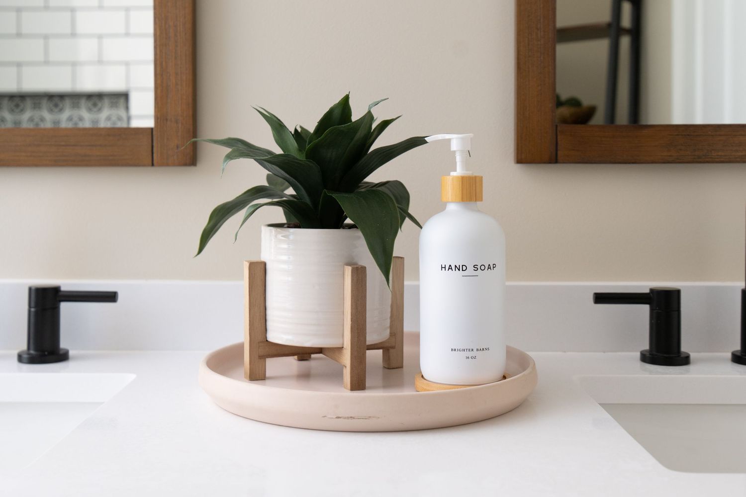 Minimalist bathroom countertop with white hand soap dispenser, potted green plant on wooden stand, and pink tray.