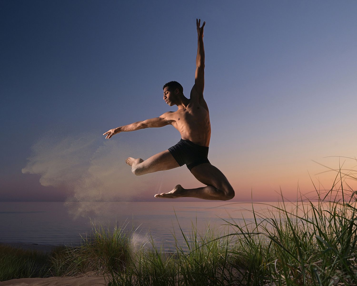 Silhouette of a dancer leaping gracefully against a sunset sky over water.