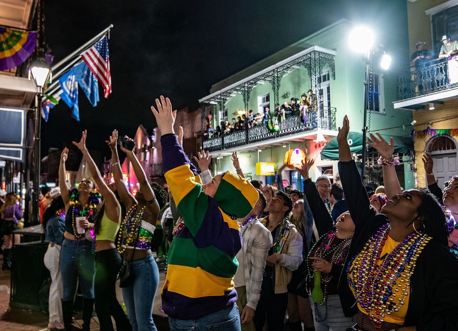 Festive Mardi Gras celebration on Bourbon Street with crowds and colorful decorative flags at night.