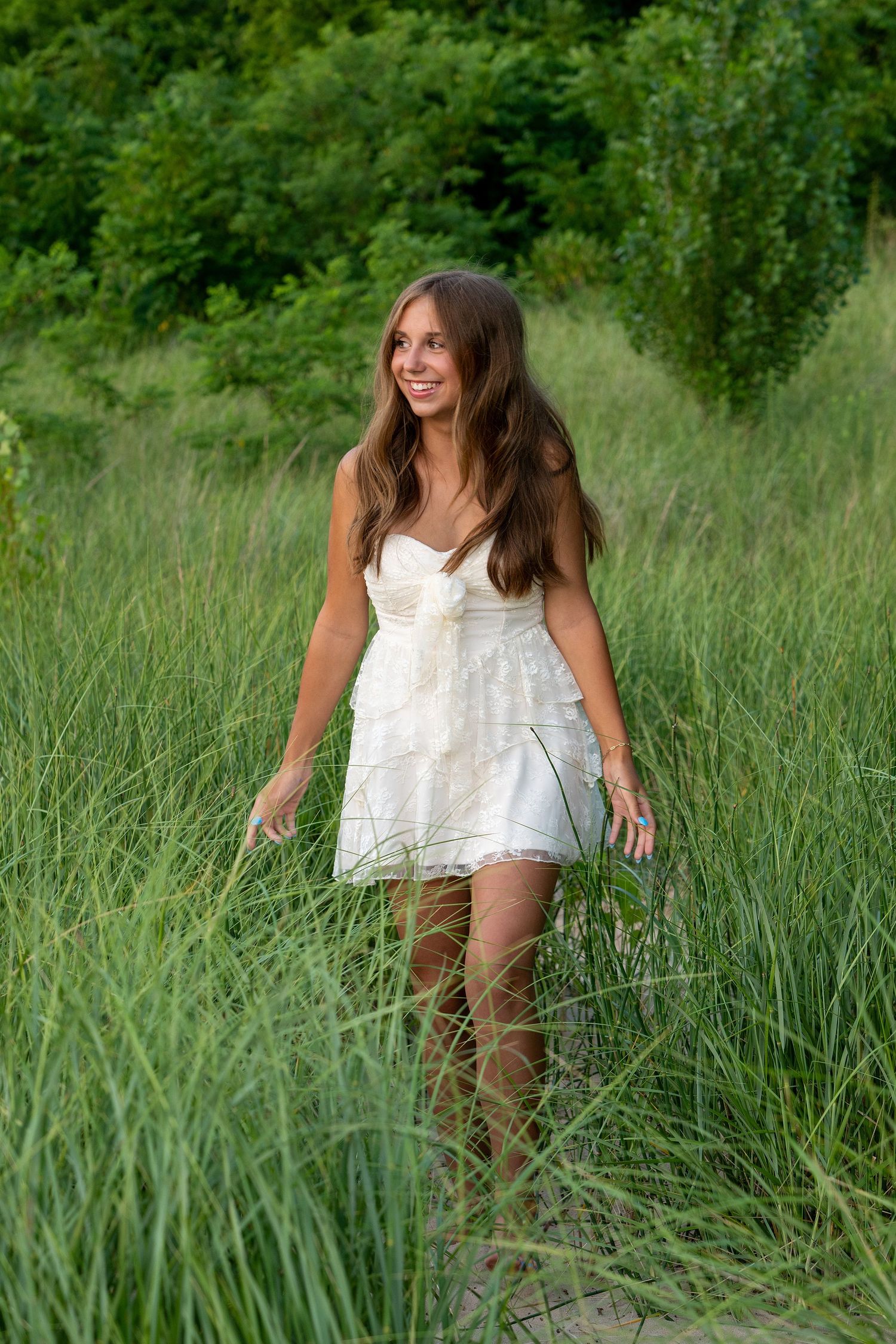 Playful summer photoshoot in a white lace dress among tall grass.