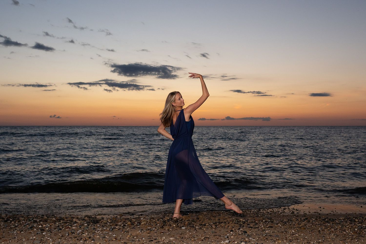 Expressive dance movement captured on beach with vibrant orange sunset sky.
