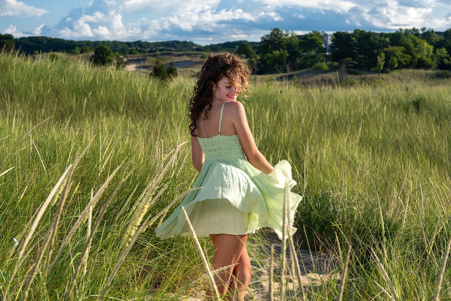 Person in white dress sitting in tall grass field under blue sky.