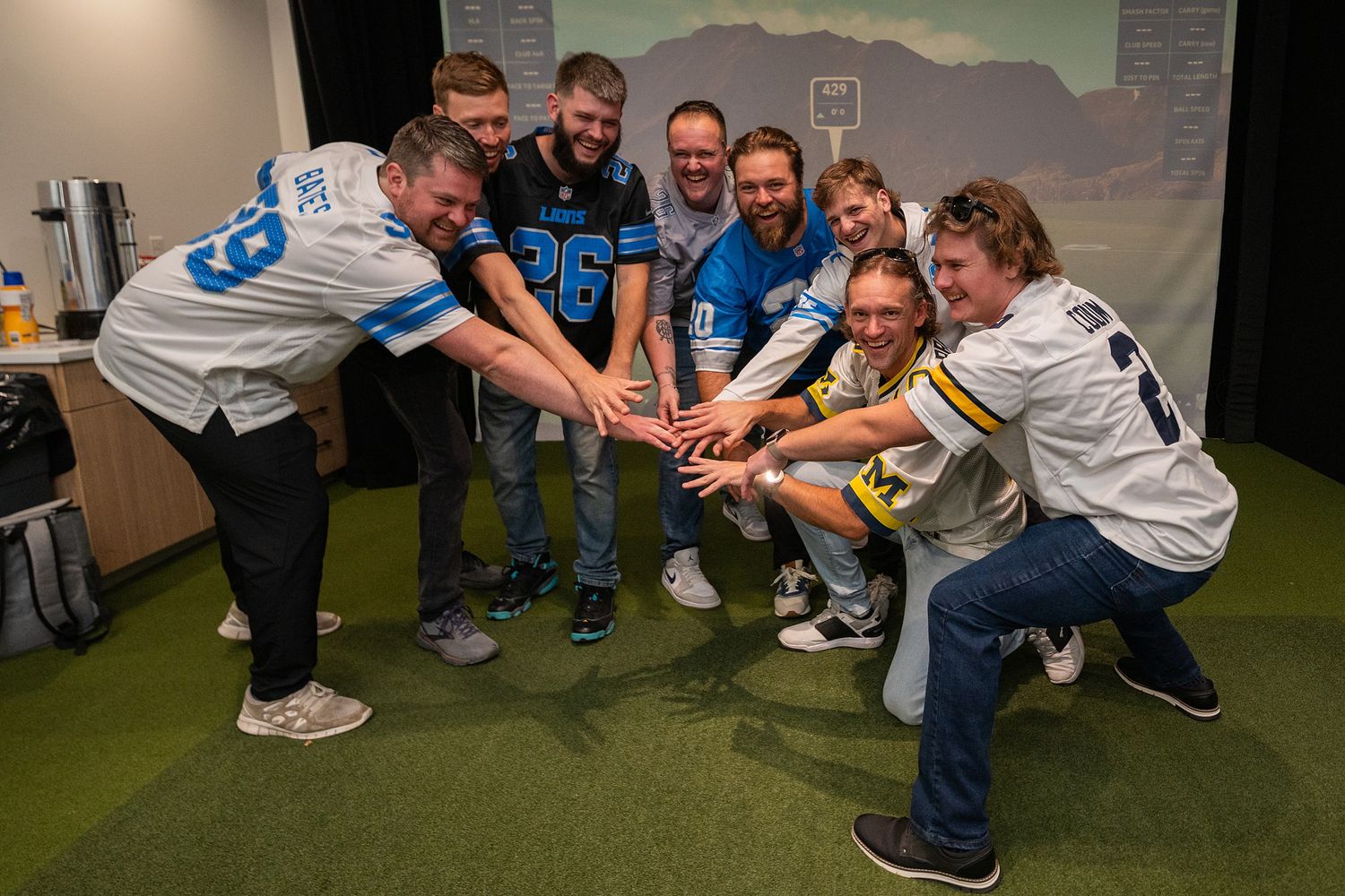 Group of friends in football jerseys joining hands together in a team huddle at an indoor sports venue.