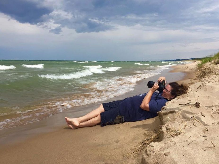 Photographer lying on beach sand capturing photos of Lake Michigan waves.
