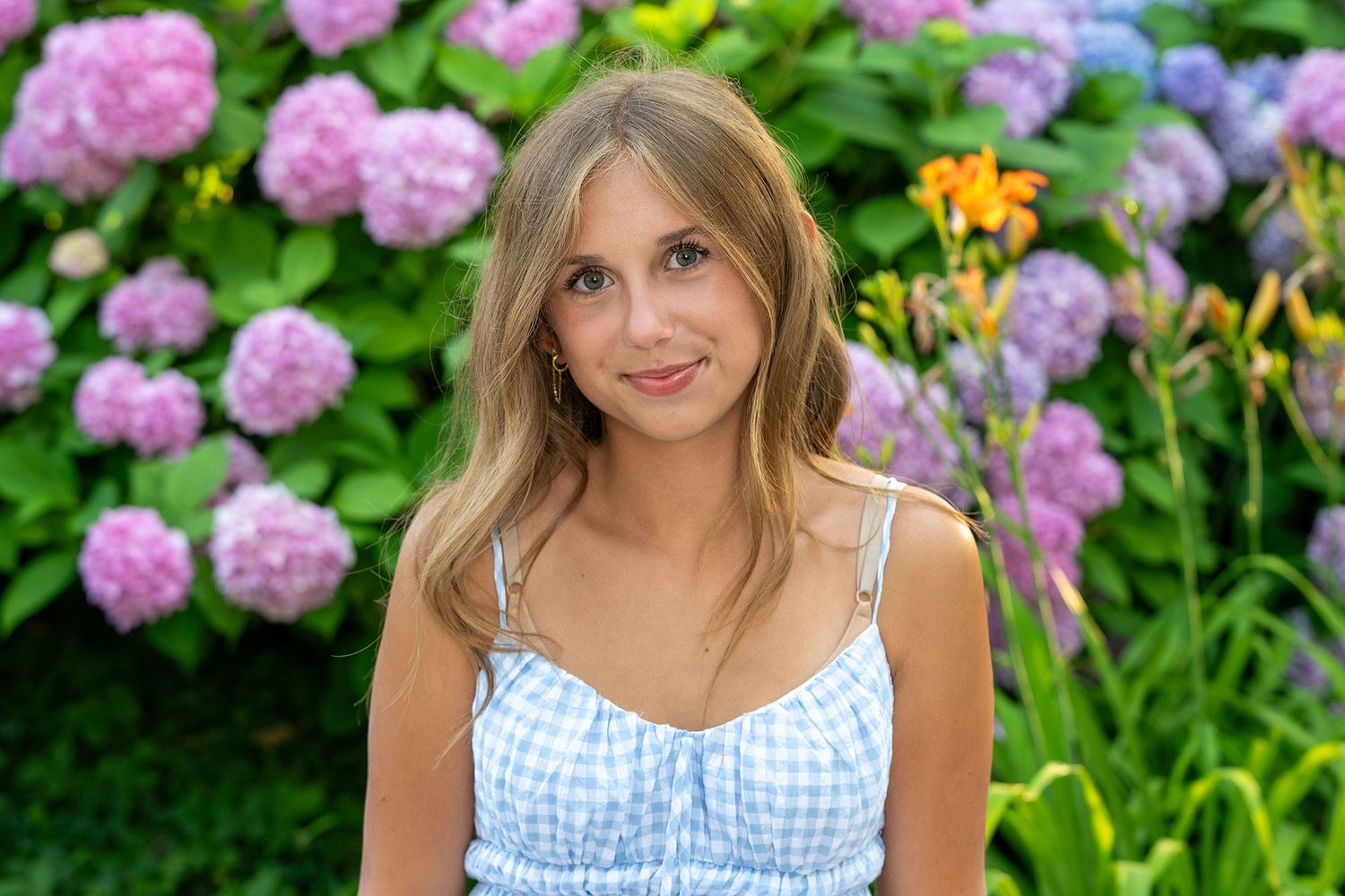 A summer photo session in a garden with pink hydrangea flowers and a blue gingham dress.