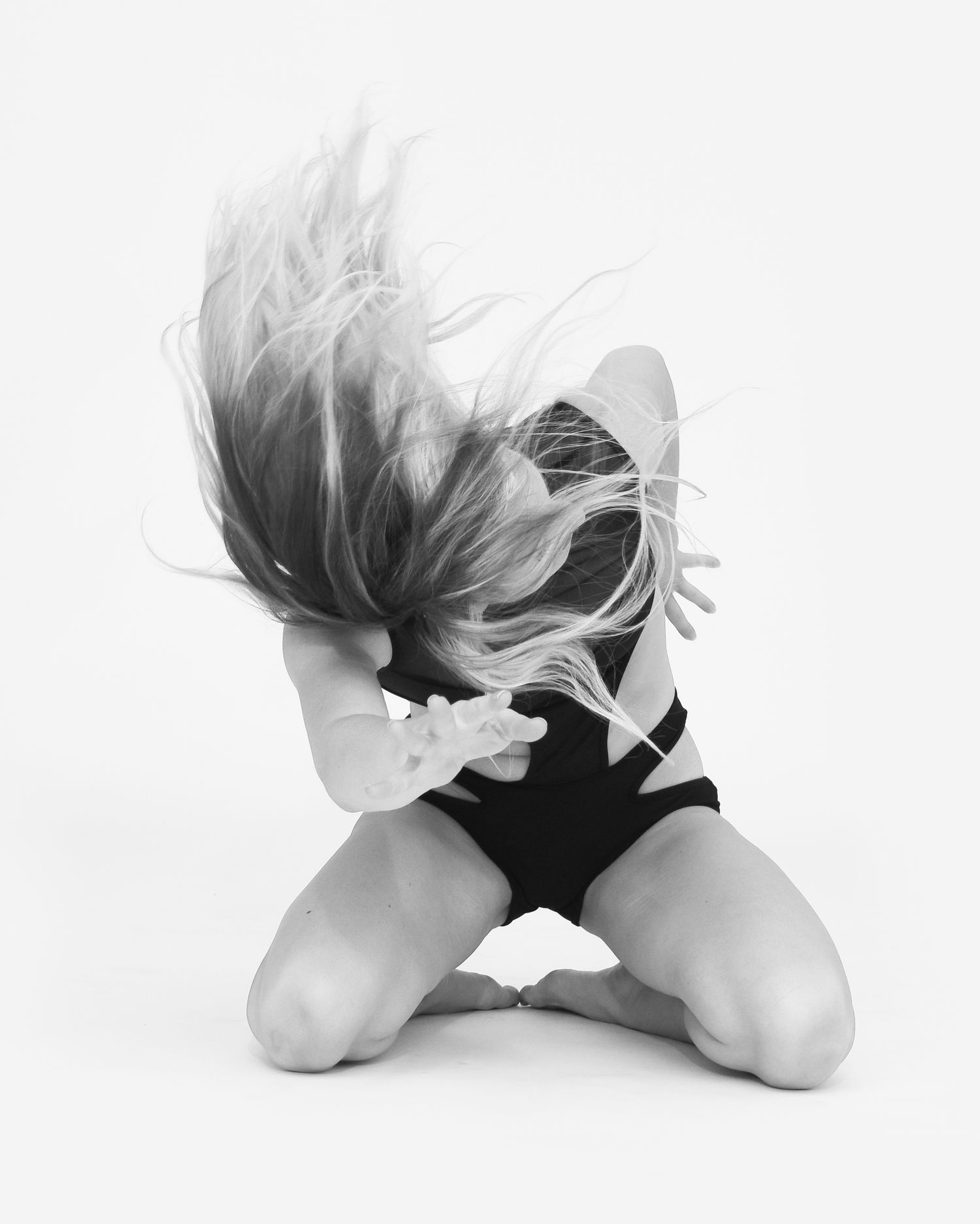 Artistic black and white photograph capturing fluid dance movement on floor with dramatic hair motion.