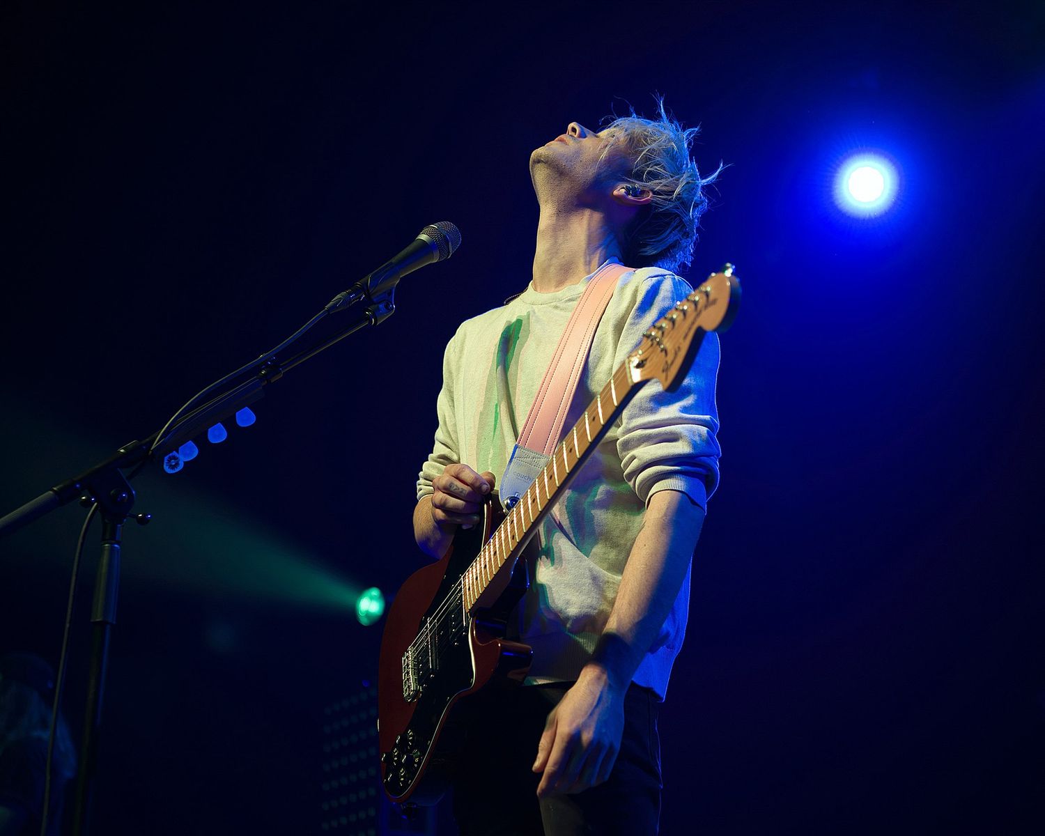 Musician playing bass guitar under blue stage lighting during passionate performance.