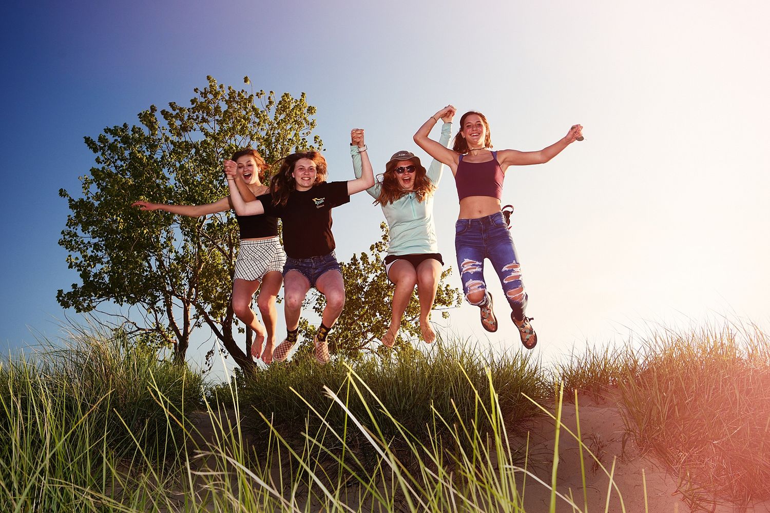 Silhouetted group jumping joyfully against sunny sky in beach grass.