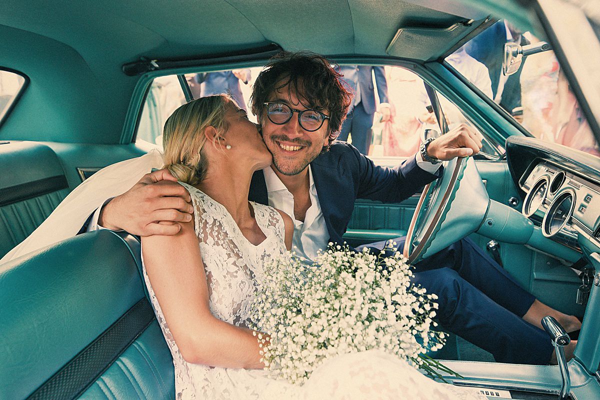 Wedding couple sitting together in car with baby's breath flowers visible.