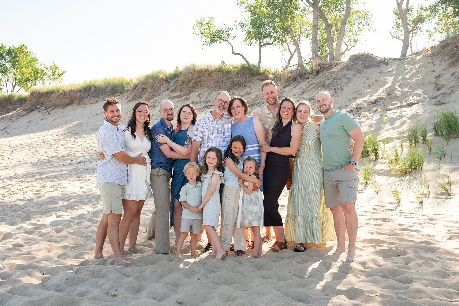 Extended family group photos taken on sandy dunes with coordinated casual outfits.