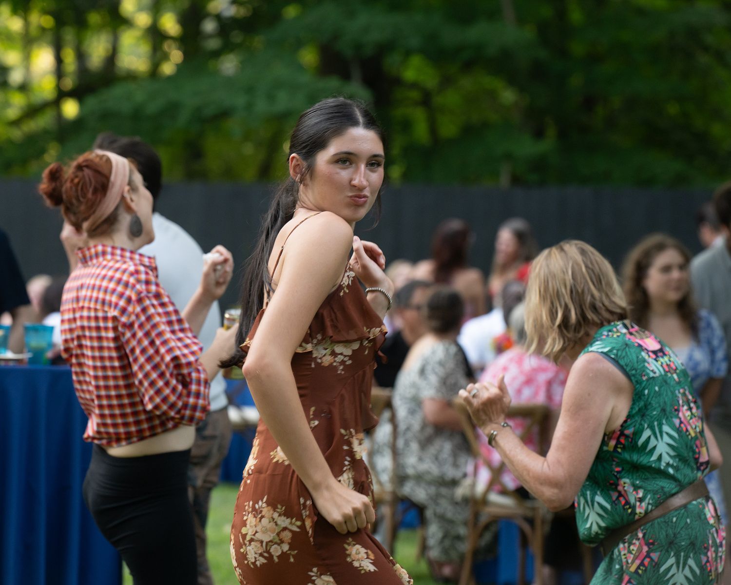 People dancing and socializing at an outdoor summer gathering with trees in the background.