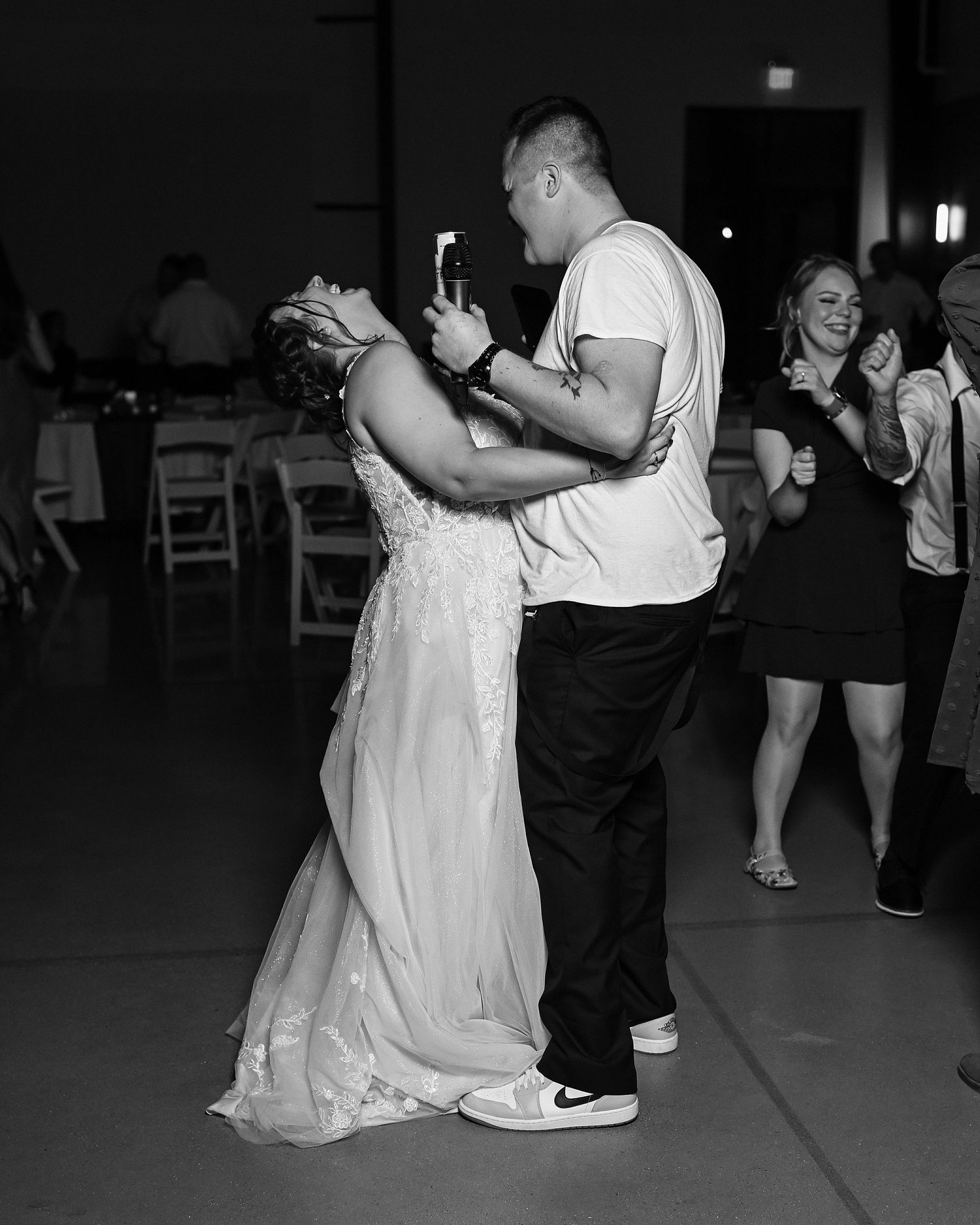 Black and white photo of bride dancing with guest holding phone at wedding reception.