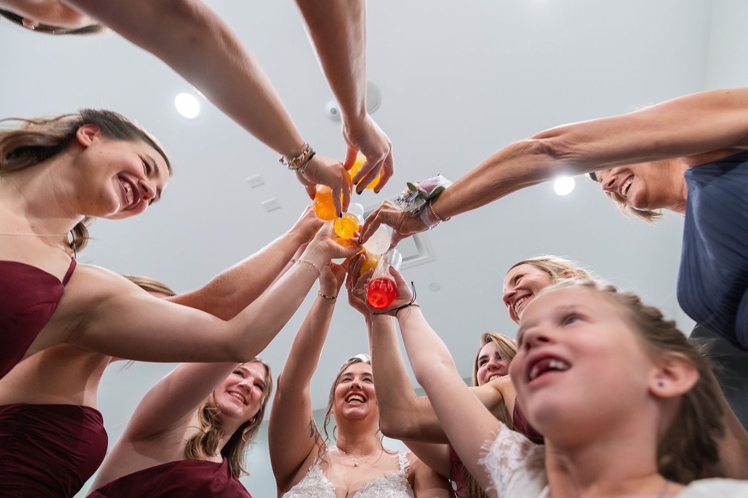 Bridal party smiling and clinking glasses in a joyful toast captured from below.