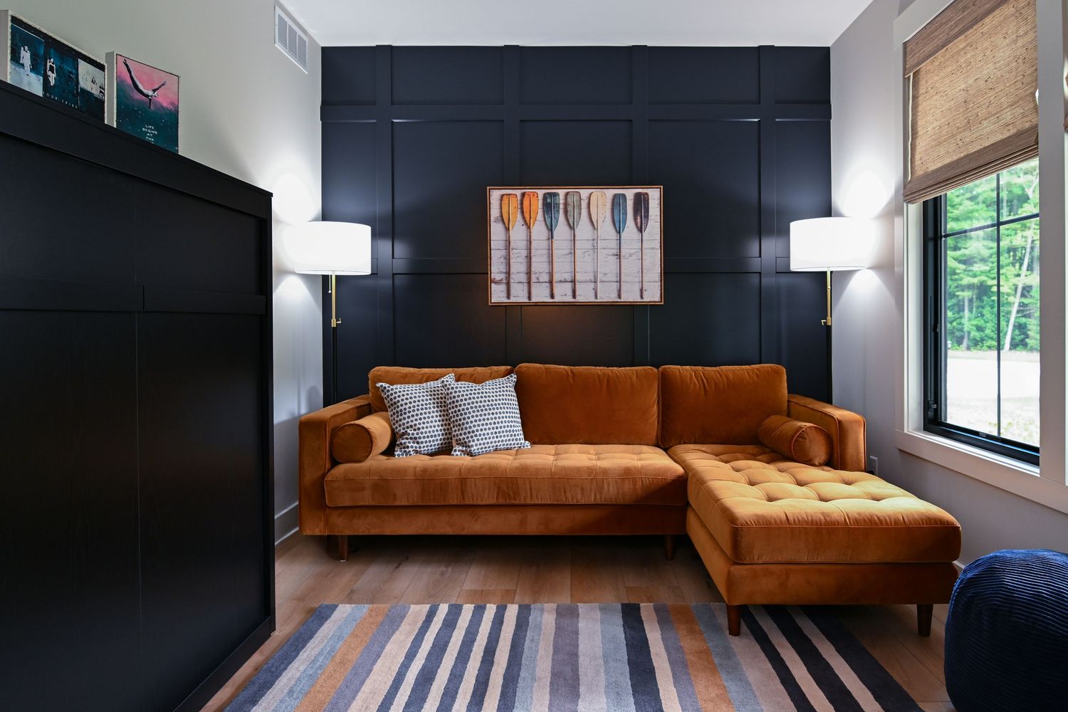 Modern living room with orange velvet sectional sofa, dark navy accent wall, striped rug, and natural wood flooring.
