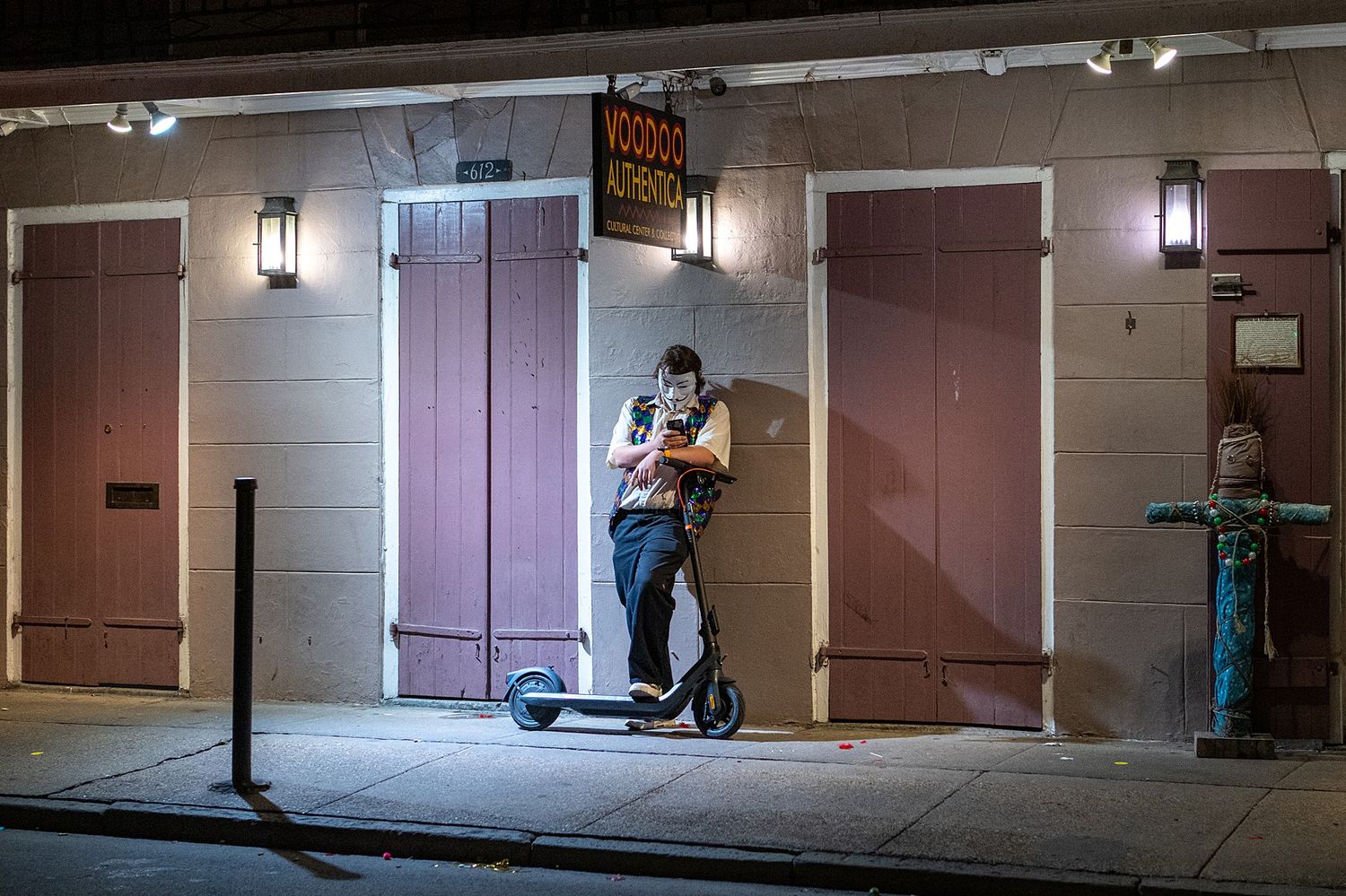 Person riding electric scooter at night along illuminated building facade.