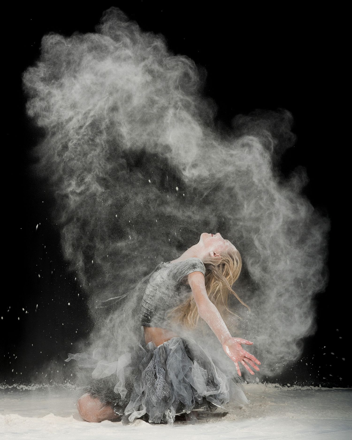 Dance performance with powder effects creating ethereal cloud-like formations against black background.