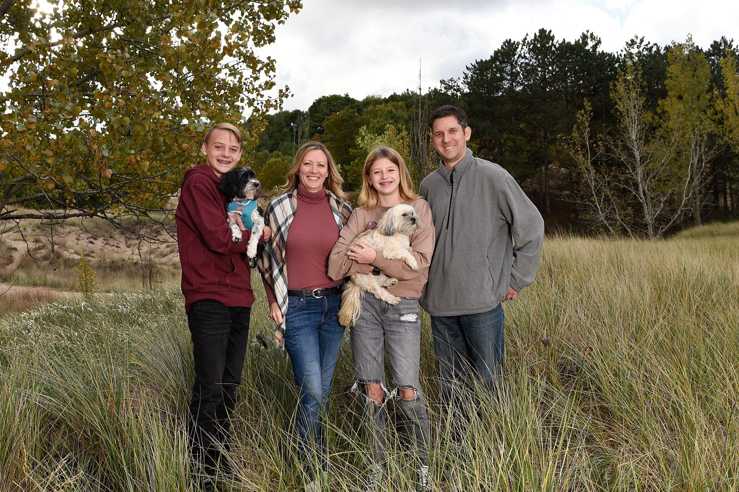 A group stands together in tall grass with autumn trees in the background during an outdoor photo session.