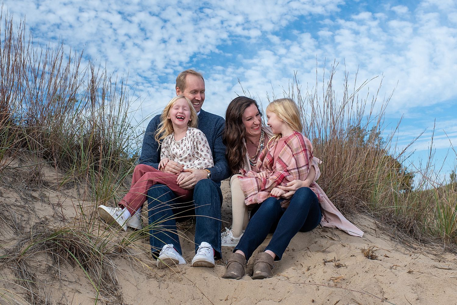 Family sitting together on sandy dunes against blue sky backdrop.