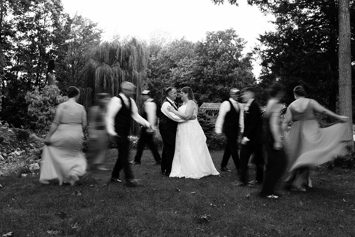 Black and white motion blur photo of wedding party dancing outdoors.