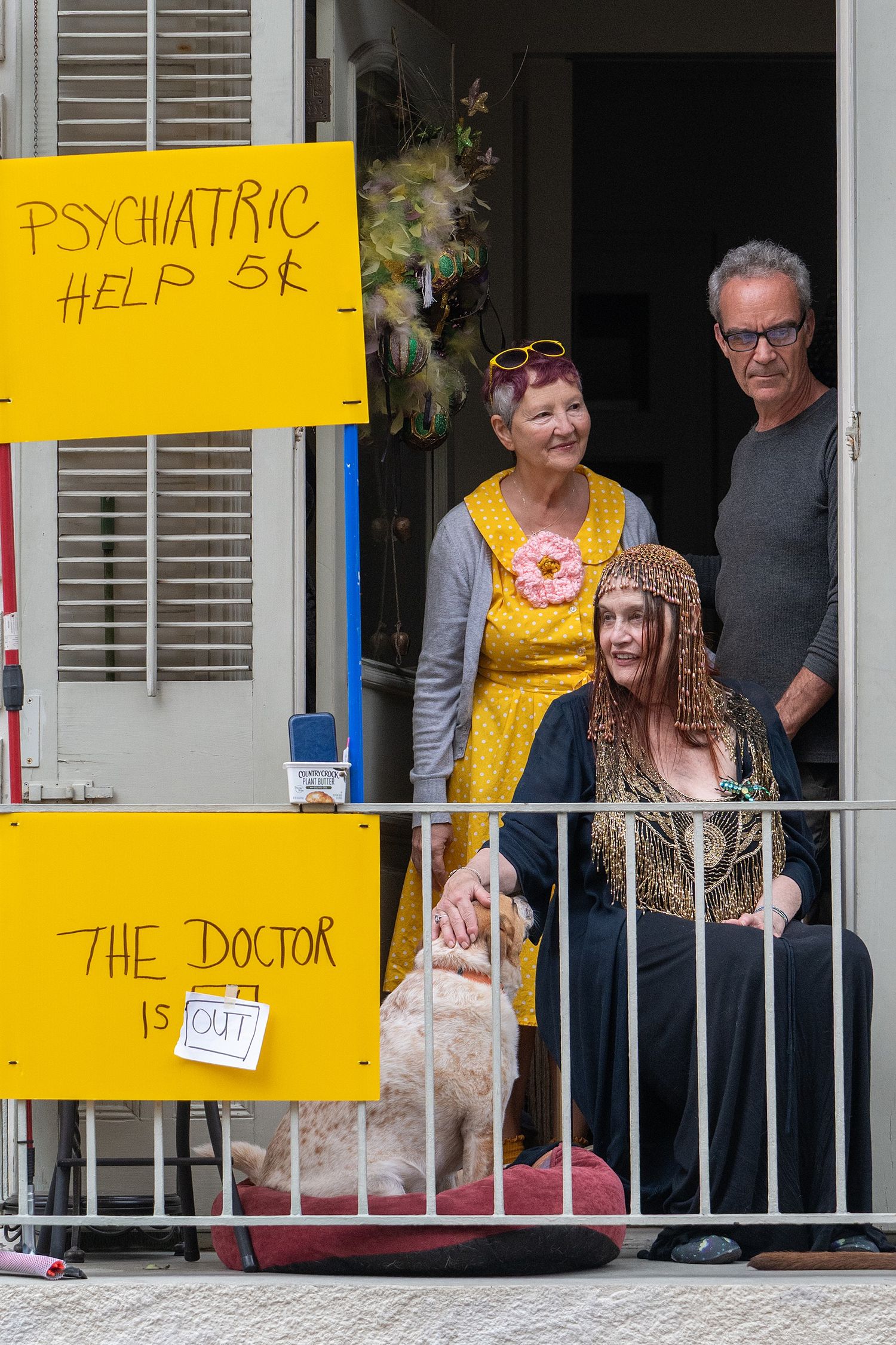 Yellow signs reading 'Psychiatric Help' and 'The Doctor' hang on a balcony during a street festival.