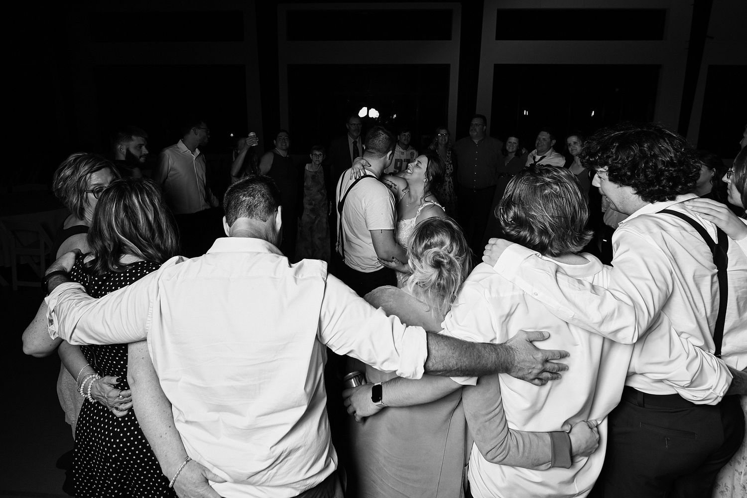 Black and white photo of wedding guests dancing together in a group at reception.