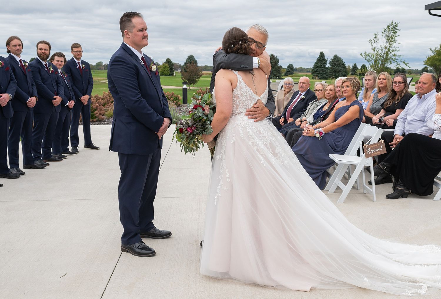 Bride receives an emotional hug from family member while groom waits at the altar.
