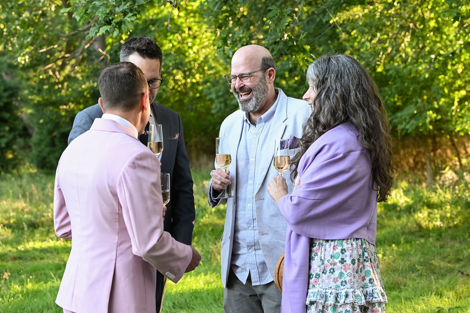 A group of people gathered outdoors in a garden setting having animated conversations on a sunny day.