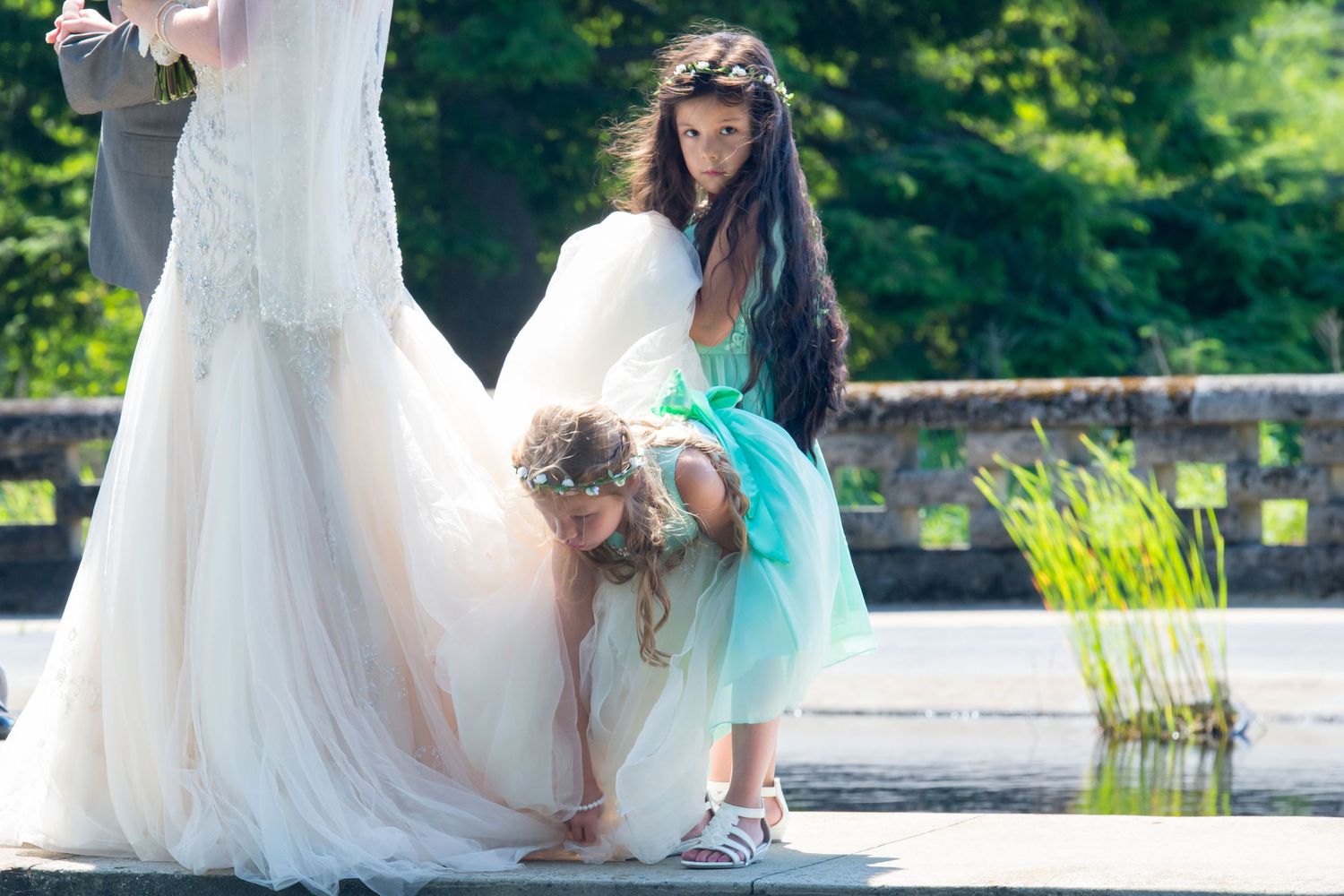Wedding party in light colored dresses poses near pond with aqua blue accents.