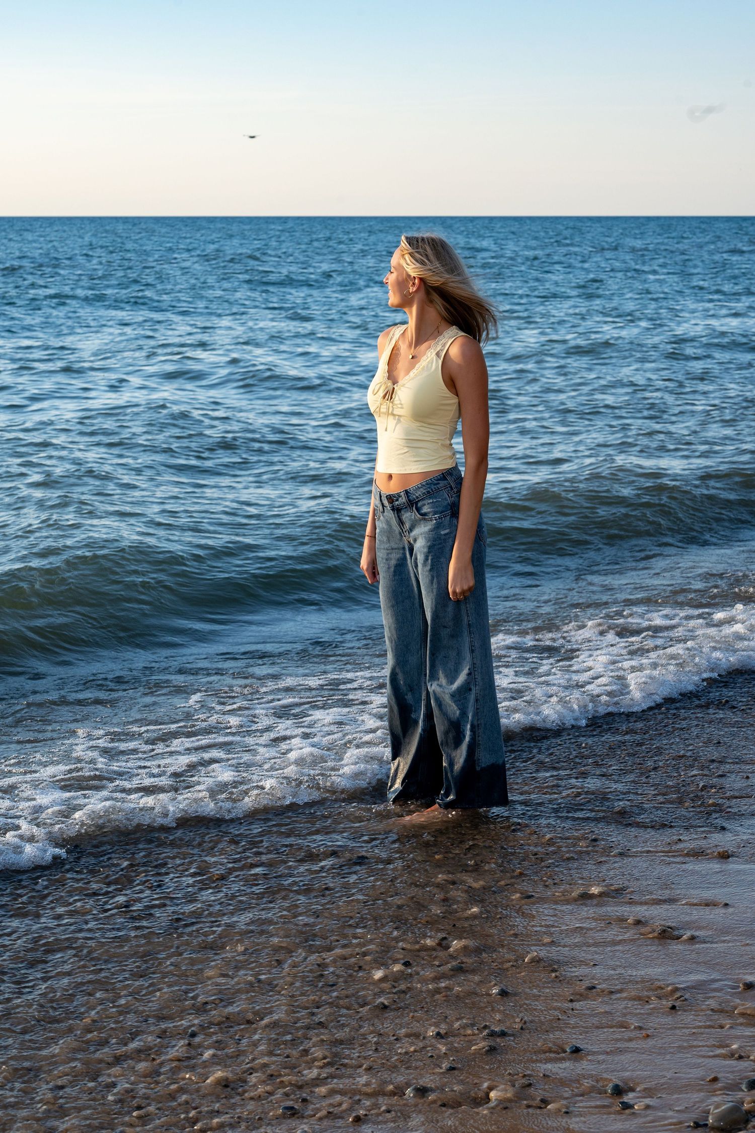 Figure standing in casual wear on a rocky beach as waves roll in during golden hour.