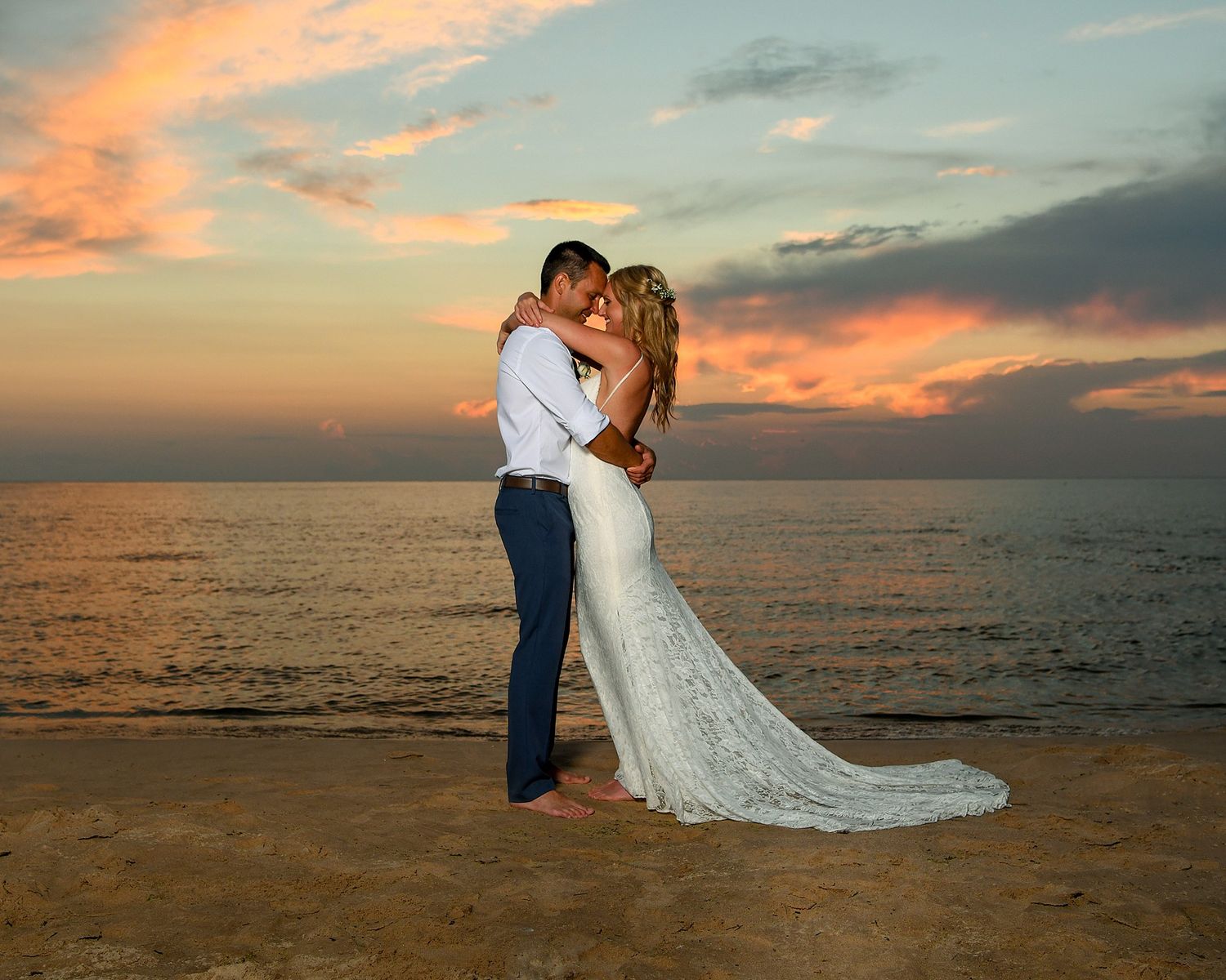 A romantic beach wedding portrait with a couple embracing against a vibrant sunset over the ocean.