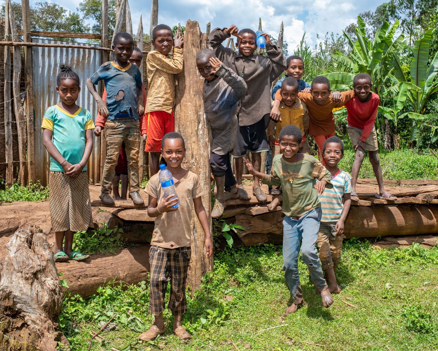 A group of children pose playfully on wooden structures in a rural village setting.