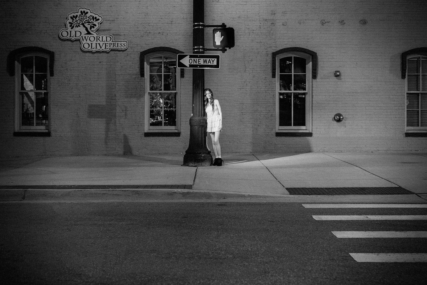 A black and white photo of someone standing by a crosswalk near a historic building.