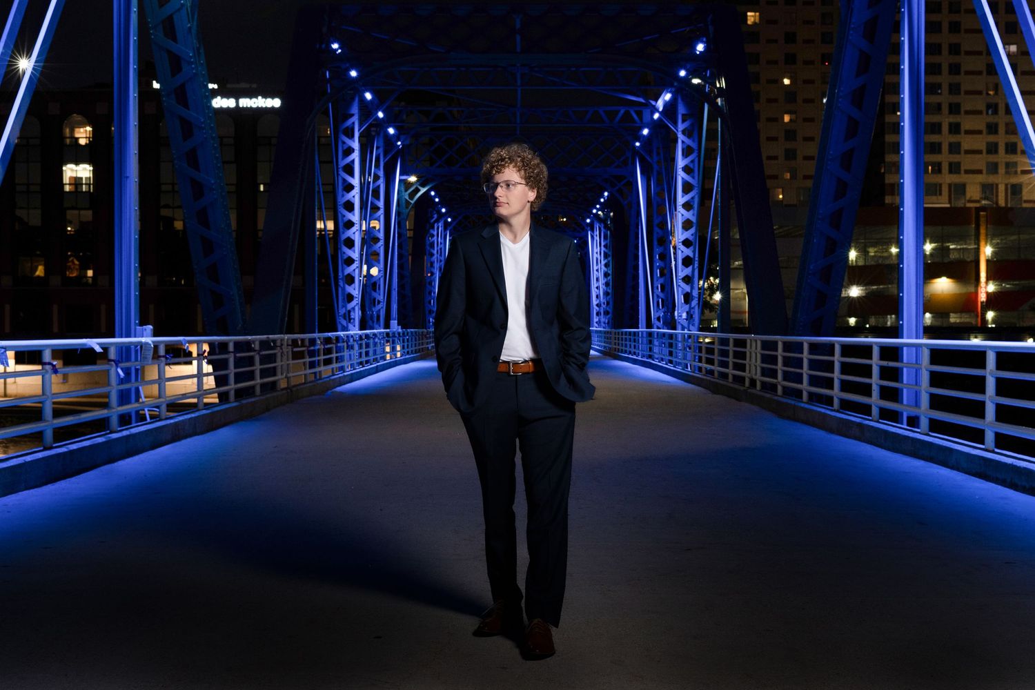 Silhouette walking on illuminated blue bridge at night in urban setting.