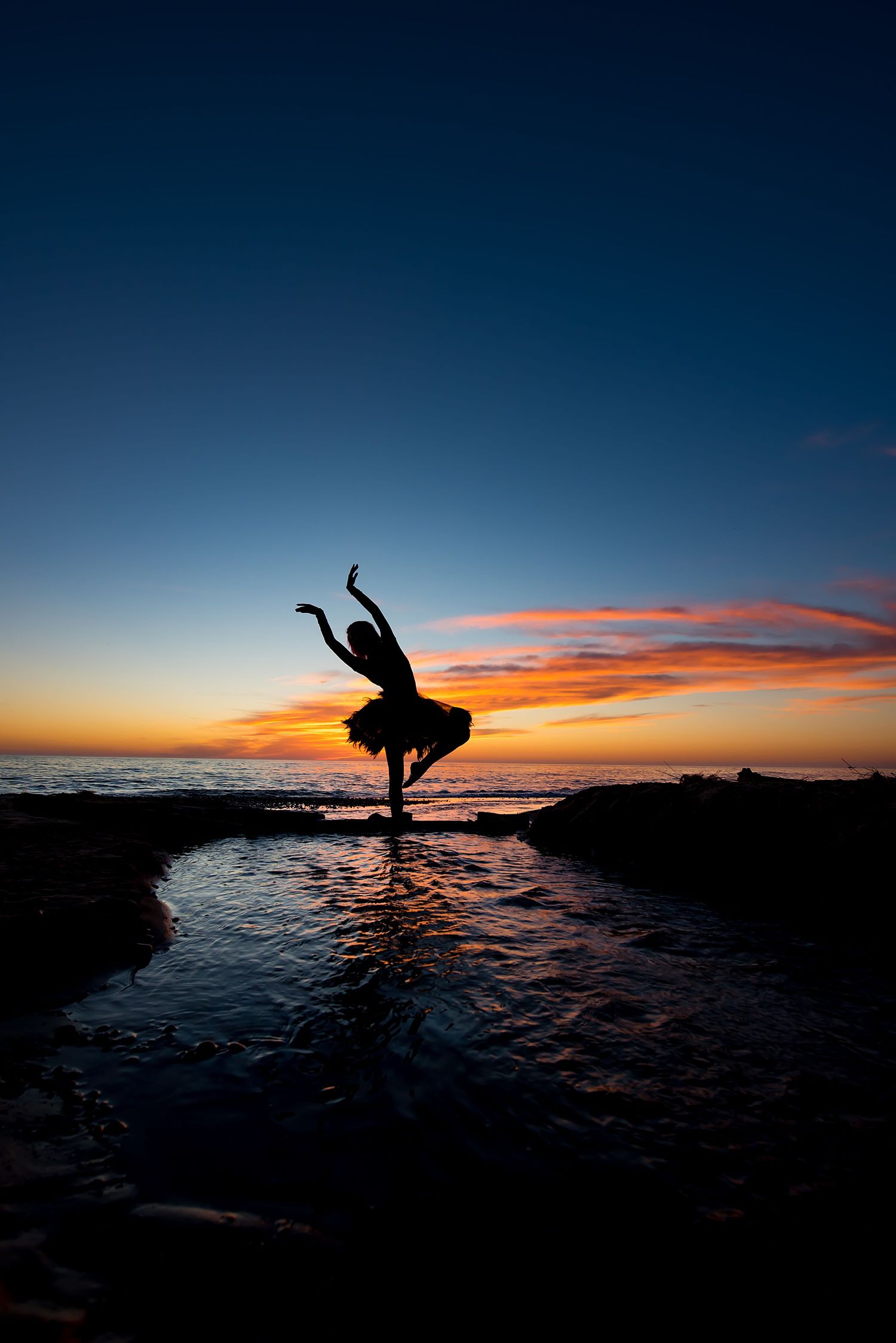 Silhouette of dancer performing at sunset against dramatic ocean backdrop.