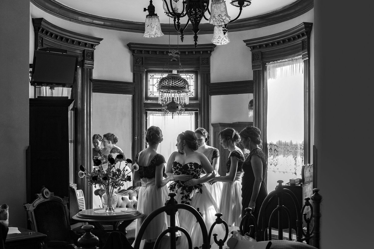 Black and white photo of bridesmaids gathered in an elegant Victorian room with chandelier before a wedding ceremony.
