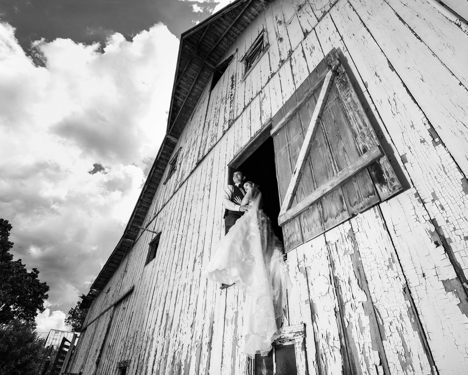 Black and white photo of a rustic white barn with dramatic clouds in the background.