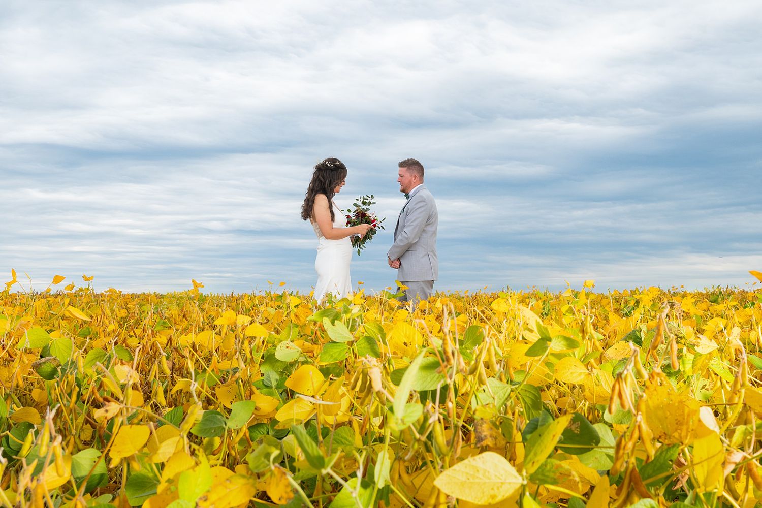Engagement photoshoot in bright yellow sunflower field under cloudy sky.