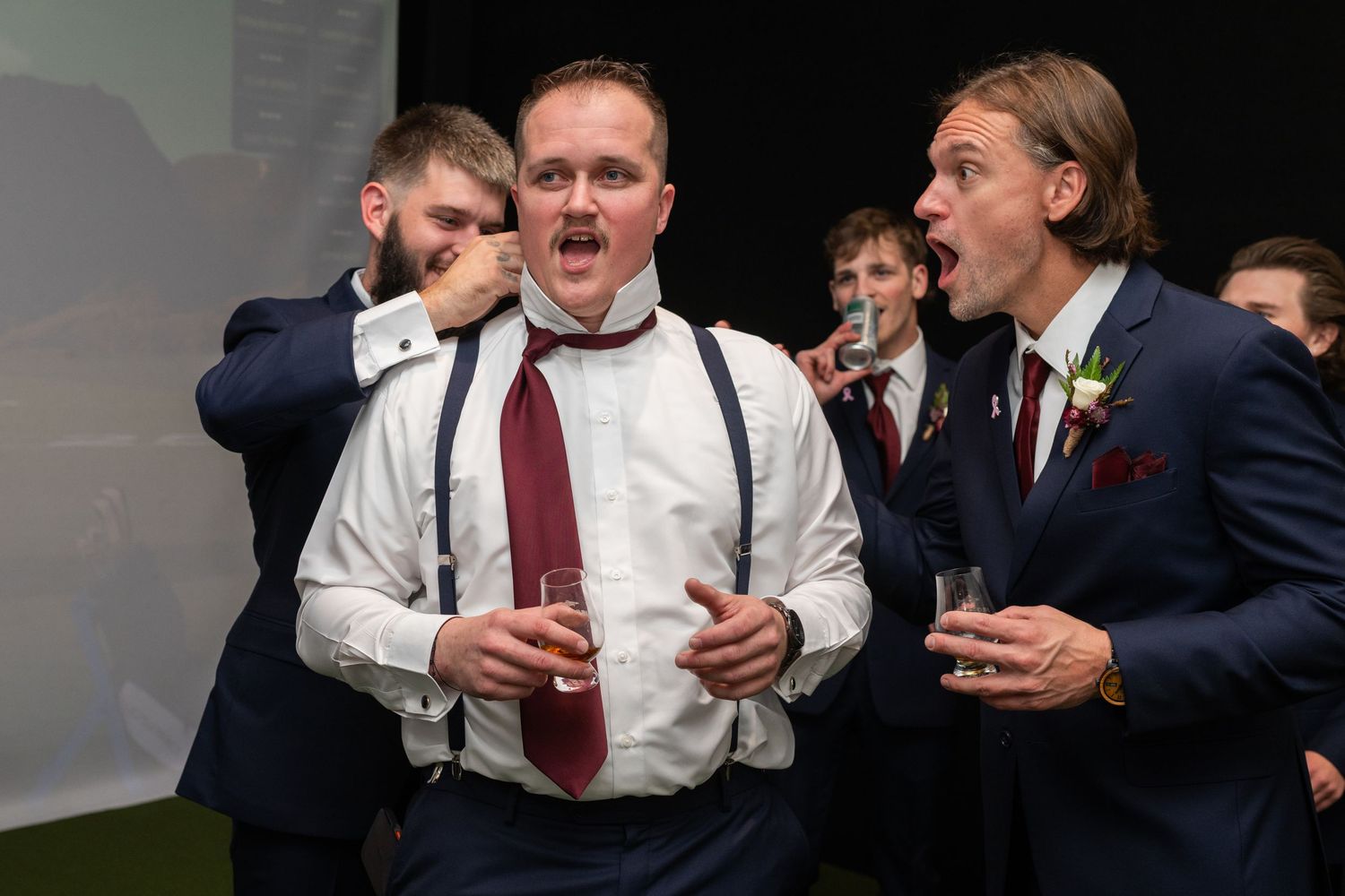 Men in suits and suspenders laughing and celebrating at a formal event, holding drinks.