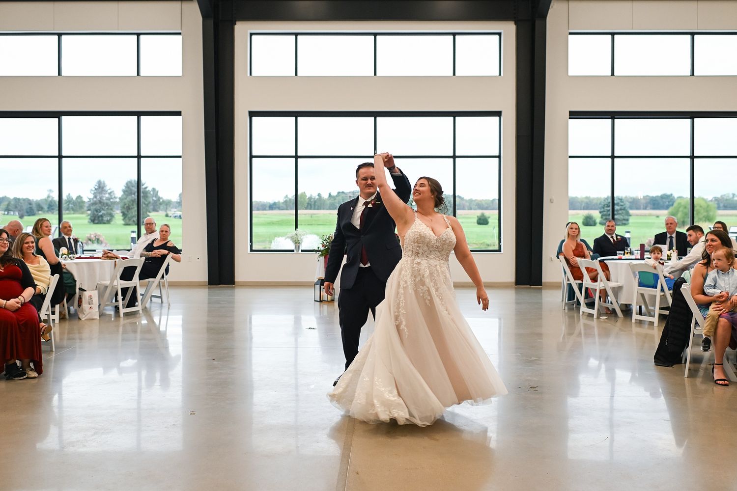 Bride and groom make grand entrance into bright modern wedding reception hall.