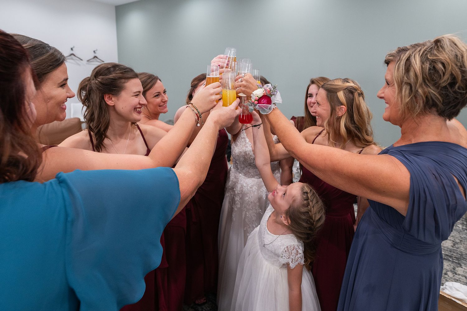 Bride and bridesmaids in burgundy and blue dresses toasting with champagne glasses at a wedding celebration.